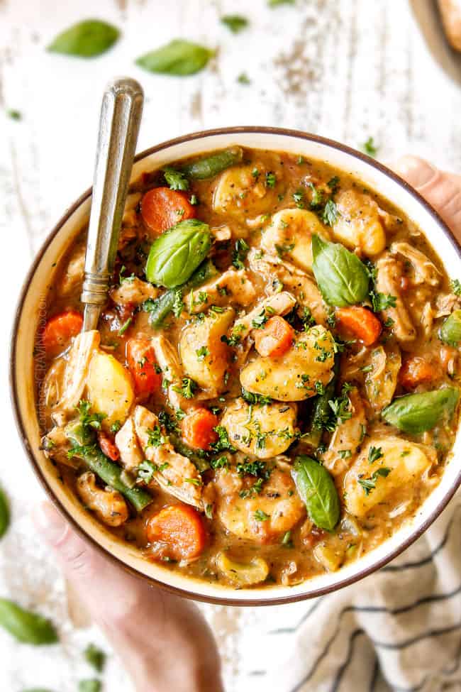 top view of two hand holding a bowl of chicken stew showing what's in it: shredded chicken, sliced carrots, sliced celery, chunks of potatoes and green beans