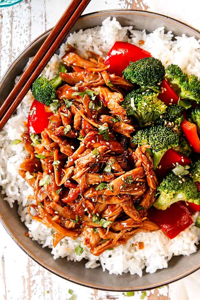 top view of garnishing slow cooker honey garlic chicken recipe in a bowl with rice with green onions and sesame seeds