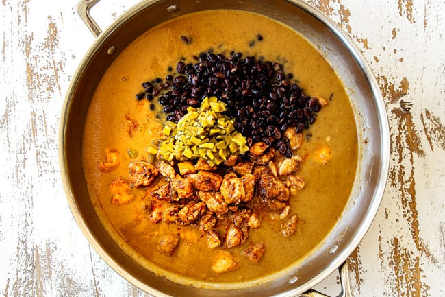 showing how to make Green Chili Chicken recipe by adding chicken broth, green chilies and black beans to the chicken in a stainless steel skillet