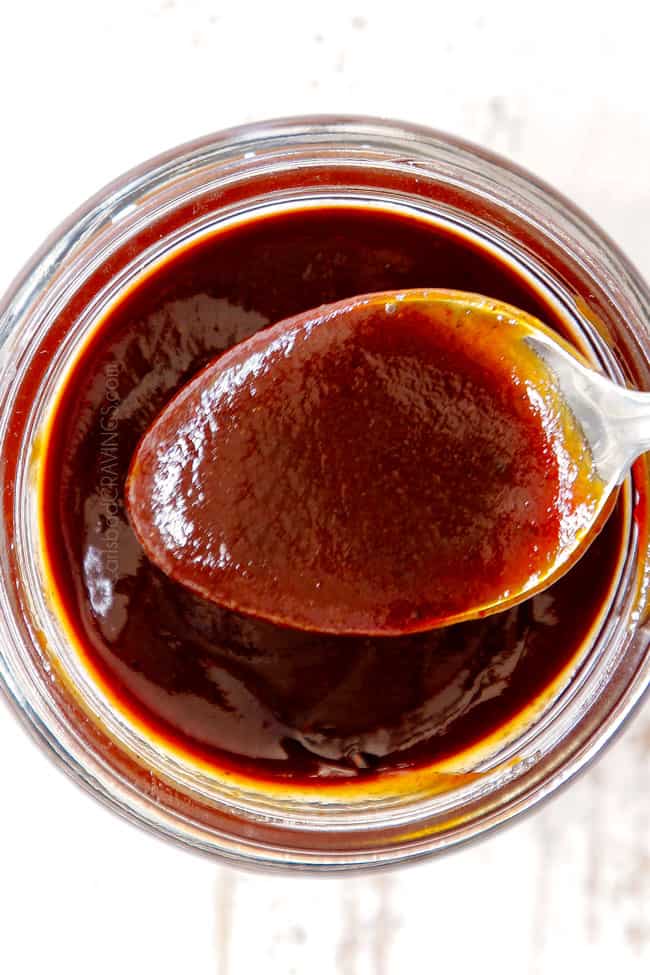 top view showing how to use homemade barbecue Sauce by dipping a spoon into the sauce in a glass mason jar.