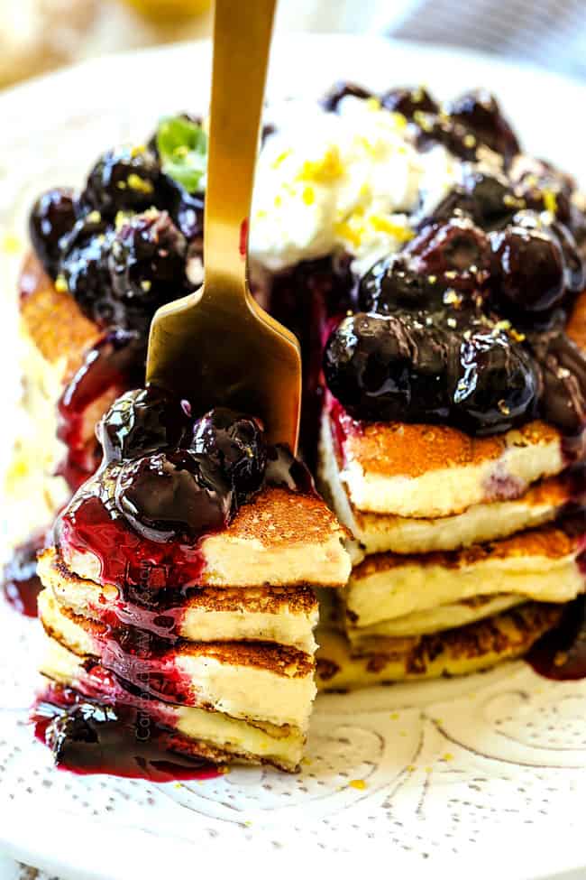 showing how to serve lemon ricotta pancakes by cutting a forkful of pancakes and piercing with a gold fork