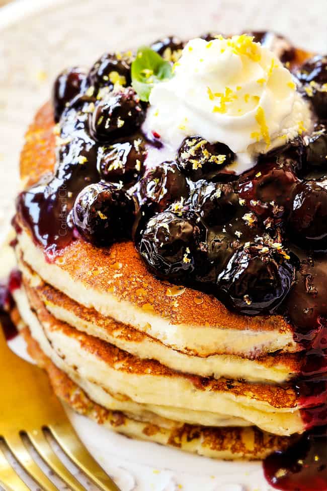 showing how to make lemon ricotta pancakes recipe by topping with whipped cream and lemon zest