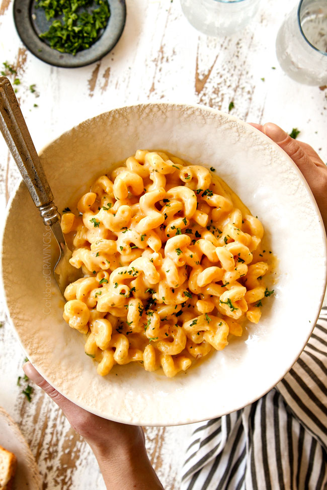 two hands holding a bowl of homemade mac and cheese showing how cheesy it is