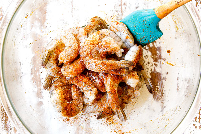 showing how to make sheet pan shrimp boil by tossing shrimp with olive oil and Old Bay seasoning