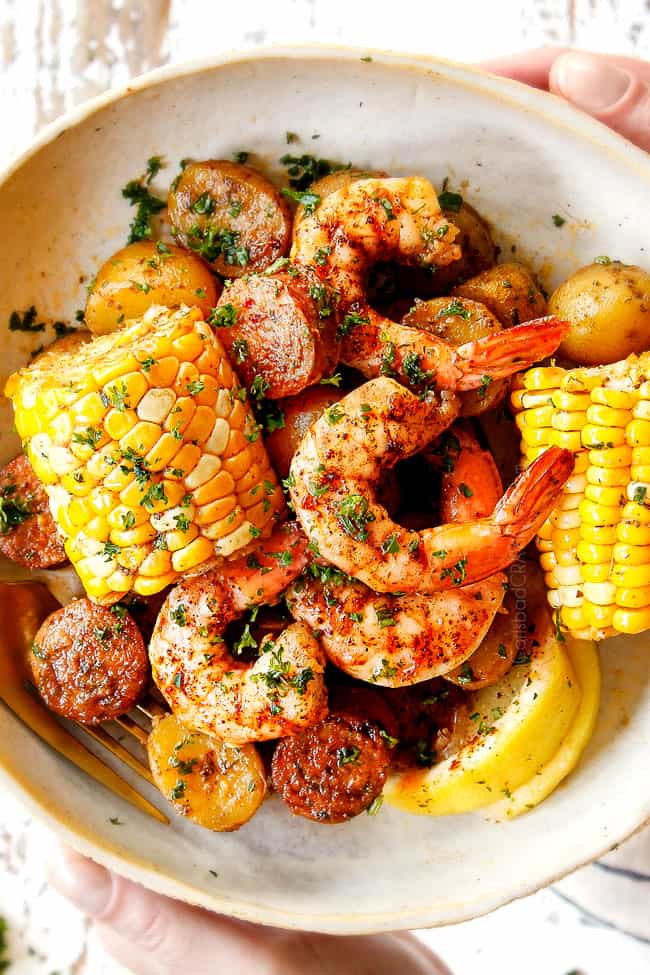 showing how to serve shrimp boil recipe by adding corn, shrimp, potatoes and sausage to a plate and drizzling with lemon juice
