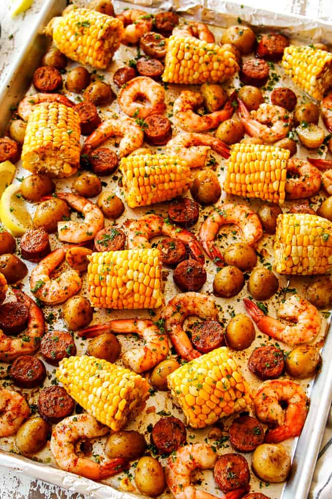 showing how to make sheet pan shrimp boil recipe by drizzling corn, potatoes, sausage and shrimp with lemon juice