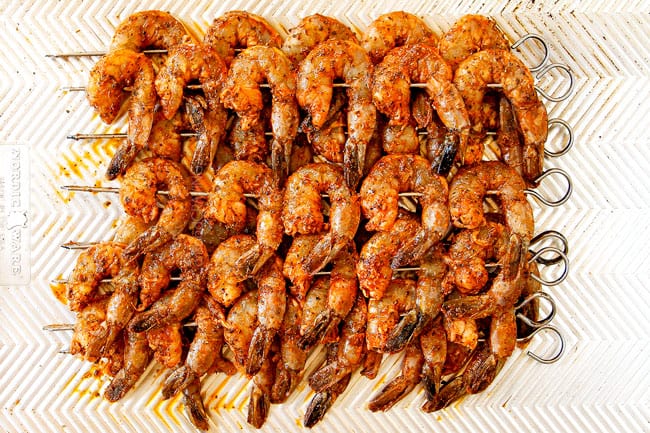 showing how to make grilled shrimp recipe by skewering marinated shrimp on metal skewers then lining on a baking sheet