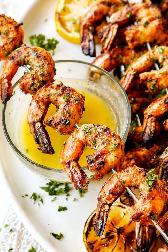 showing what to serve grilled shrimp recipe by placing a skewer over a glass bowl of lemon parsley butter