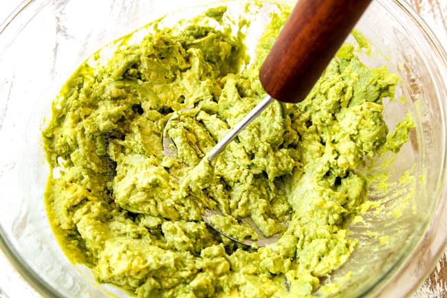showing how to make homemade guacamole by mashing avocados with an avocados masher in a glass bowl