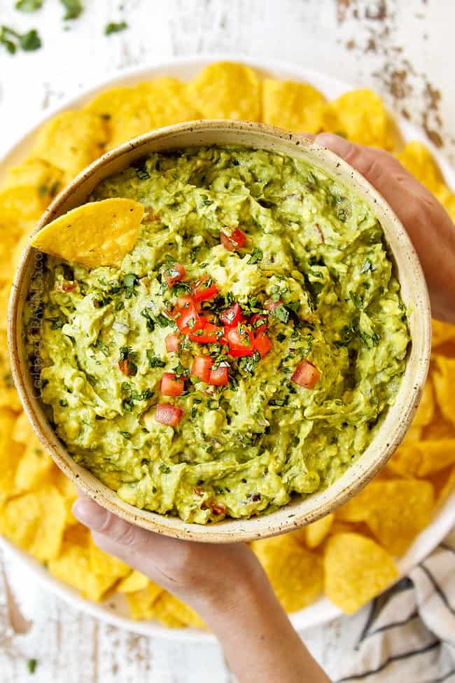 showing the texture of chunky guacamole by holding a bowl up with two hands