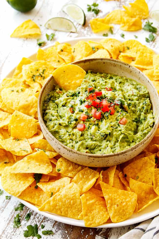 showing how to serve homemade guacamole by adding to a tan bowl and serving with tortilla chips