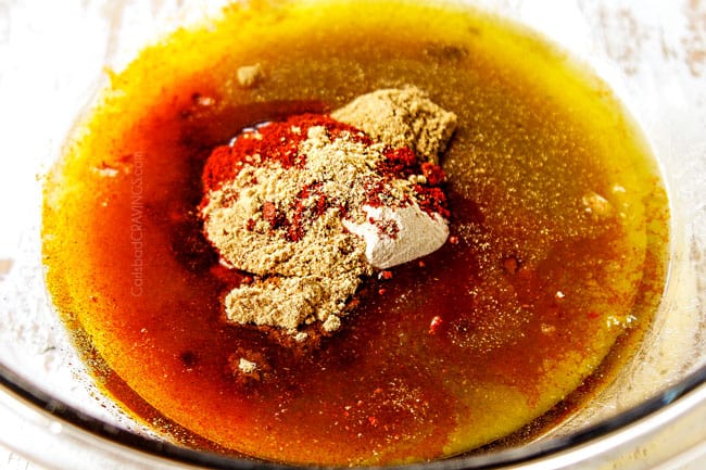 showing how to make Honey Sriracha Chicken by whisking honey, sriracha, olive oil, lime juice and seasonings together in a glass bowl