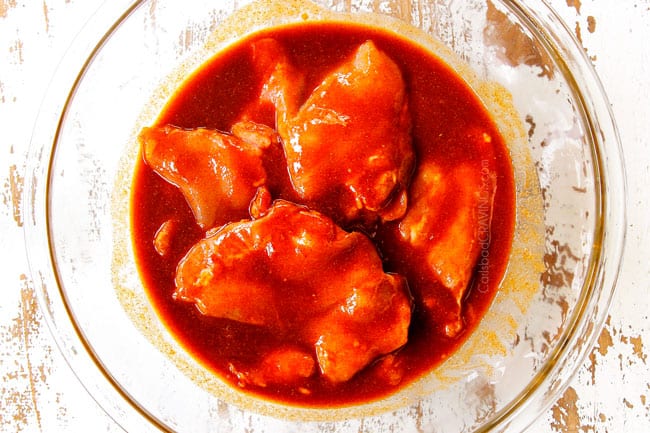 showing how to make Honey Sriracha Chicken by adding raw boneless skinless chicken thighs to marinade in a glass bowl
