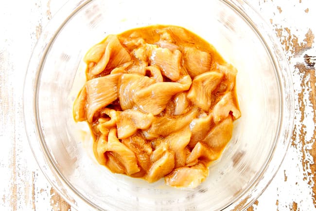 showing how to make Hunan chicken by adding thinly sliced chicken to a glass bowl with marinade ingredients
