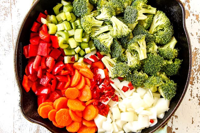 showing which vegetables you add to Hunan style chicken by adding broccoli, carrots, celery, carrots, bell peppers and chili peppers to a cast iron skillet in separate groups