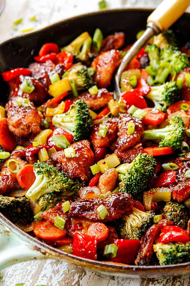 showing how to make Hunan chicken by adding stirring veggies, chicken and Hunan sauce together until combined in a cast iron skillet