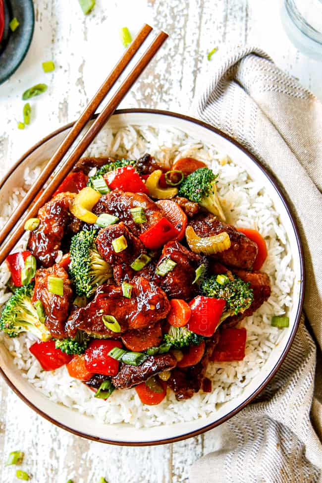 showing how to serve Hunan chicken with a top view of chicken and veggies in a bowl with rice, garnished by green onions with chopsticks on the side