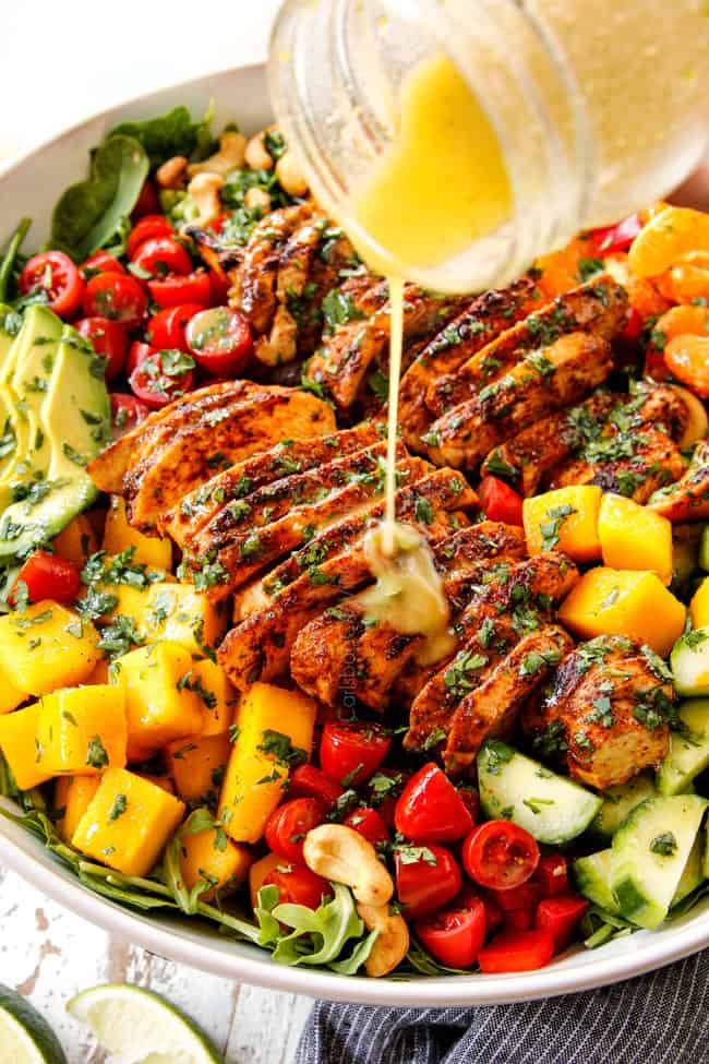 showing how to make mango salad by pouring mango salad dressing over the salad in a white bowl