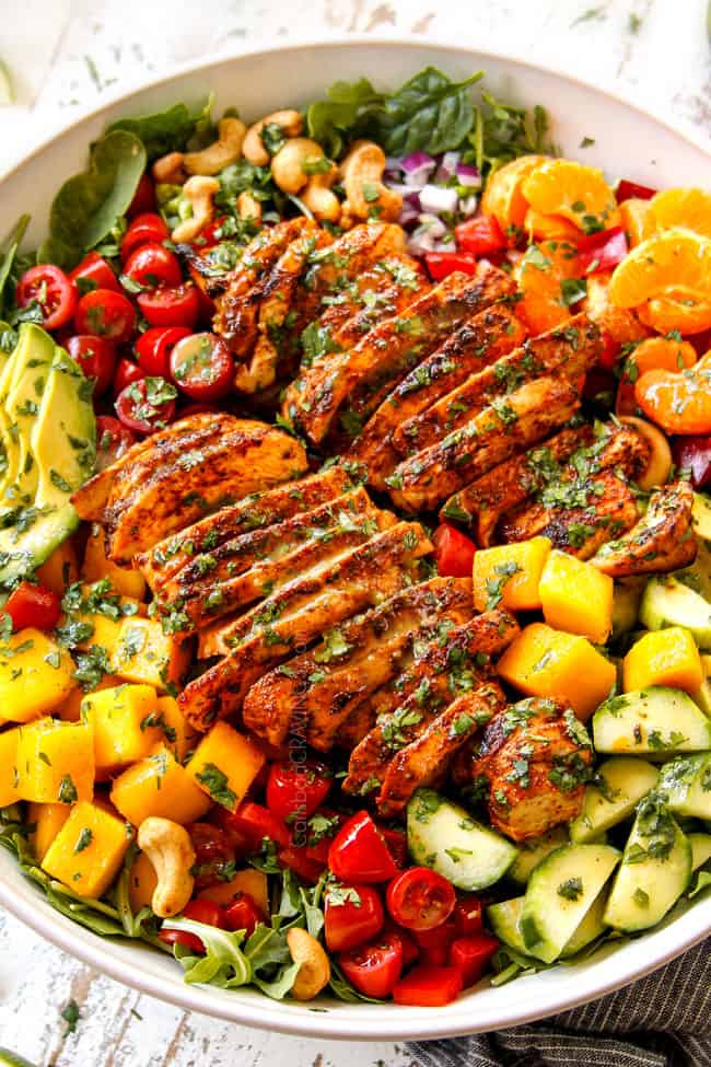 showing how to make mango salad by adding cilantro, tomatoes and oranges to a bowl