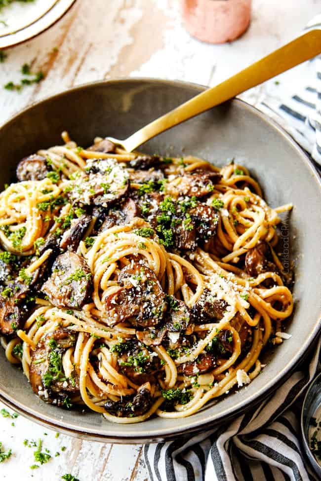 showing how to serve Mushroom Pasta by adding it to a bowl and garnishing with Parmesan