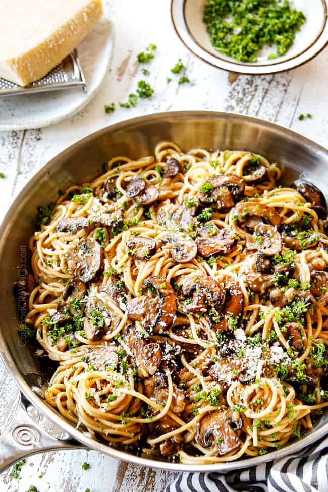 showing how to make Creamy Mushroom Pasta in a stainless steel skillet by garnishing with fresh Parmesan and parsley