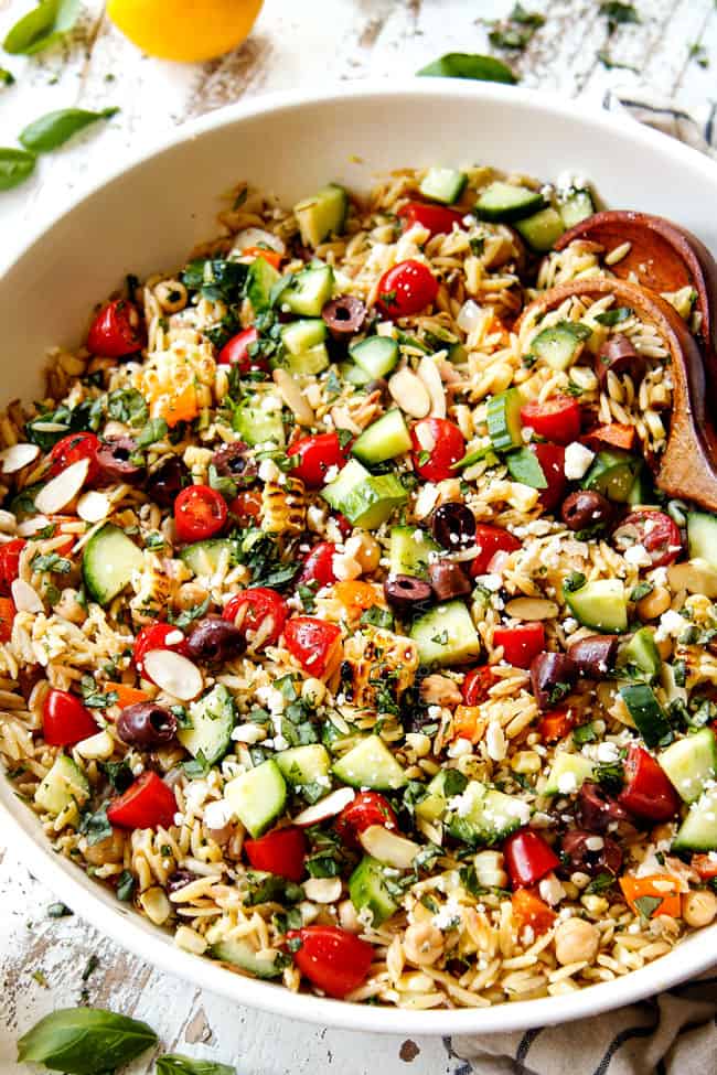 showing how to make orzo pasta by adding orzo, veggies and dressing to white bowl