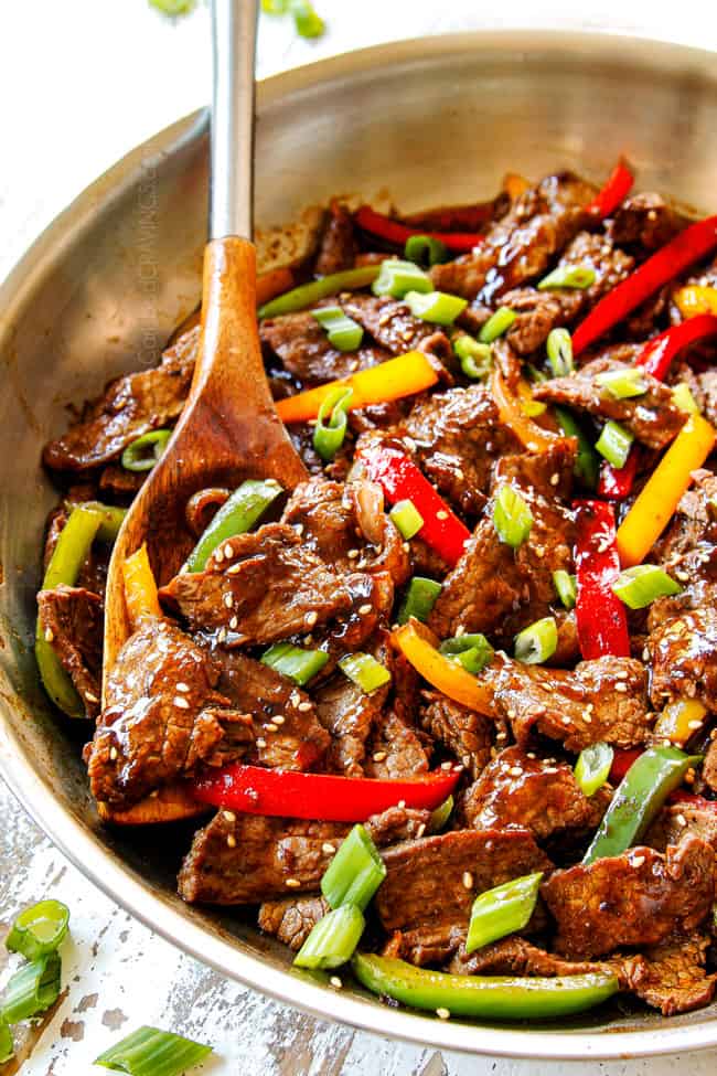 showing how to make Chinese Pepper Steak by combining steak, bell peppers and stir fry sauce in a stainless steel pan with a wooden spoon