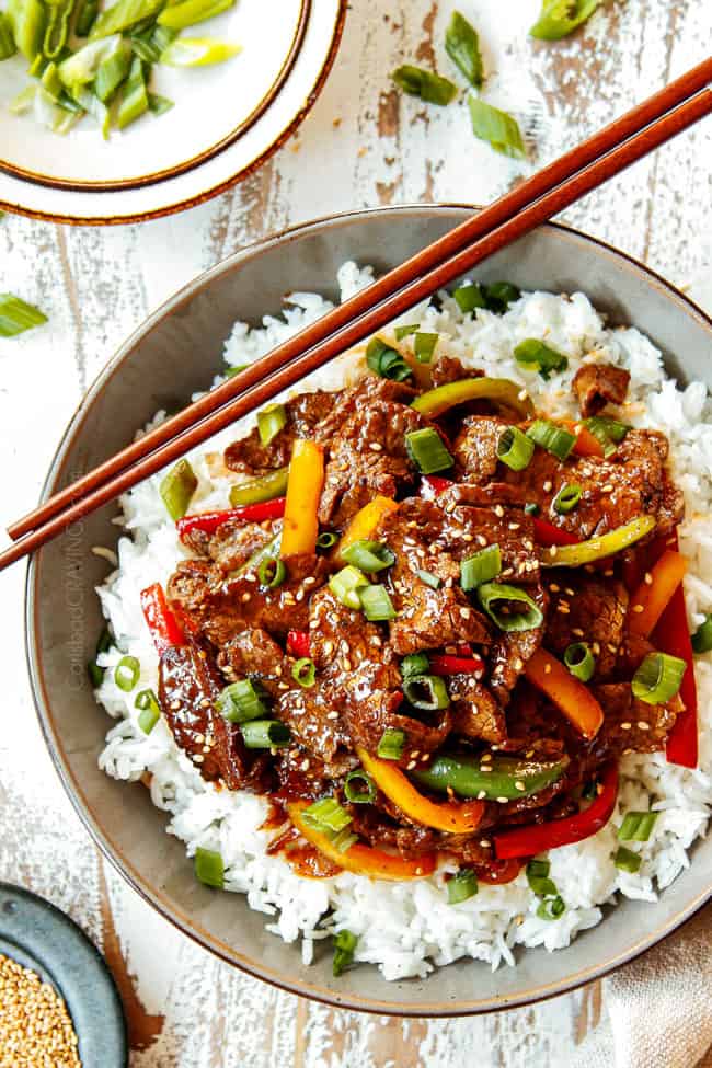top view of pepper steak in a bowl garnished with green onions and sesame seeds
