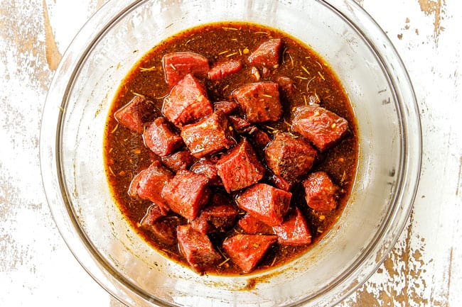 showing how to make steak kabobs by adding cubed top sirloin to a glass bowl in the steak marinade