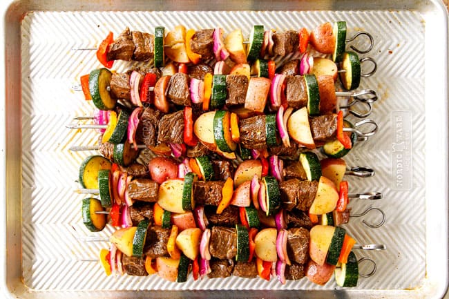 showing how to make steak kabobs by assembling steak and vegetables onto skewers and stacking on a baking sheet