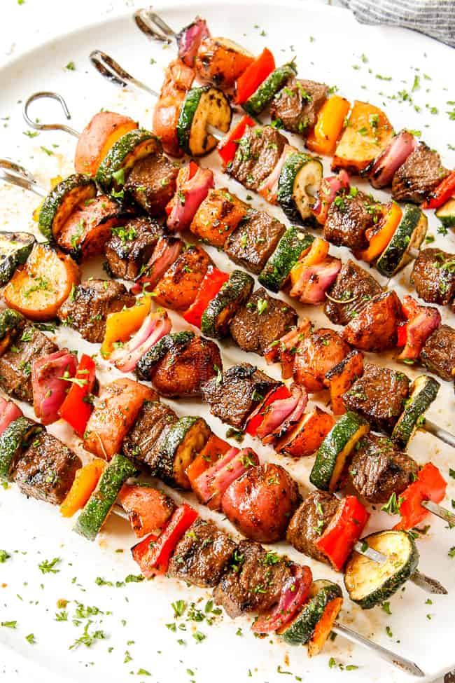 beef kabobs that have been marinated lined in a row on a white platter
