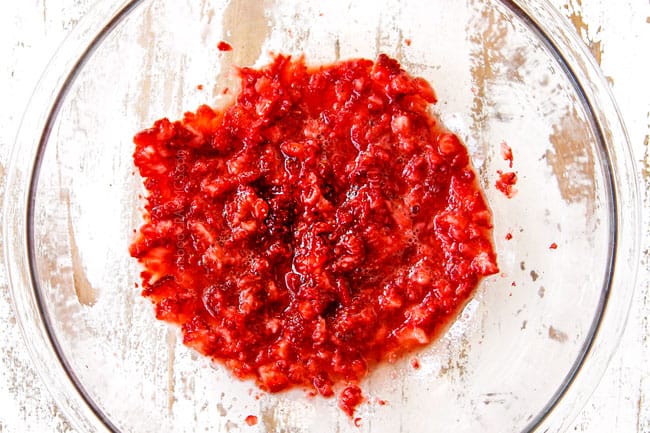 showing how to make Strawberry Shortcake by adding whole strawberries to a glass bowl and mashing