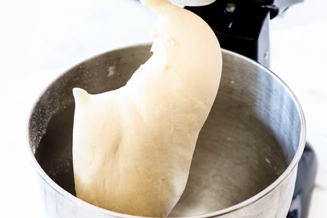 showing how to make pizza dough by mixing dough in a mixing bowl until it pulls away from the sides of the bowl