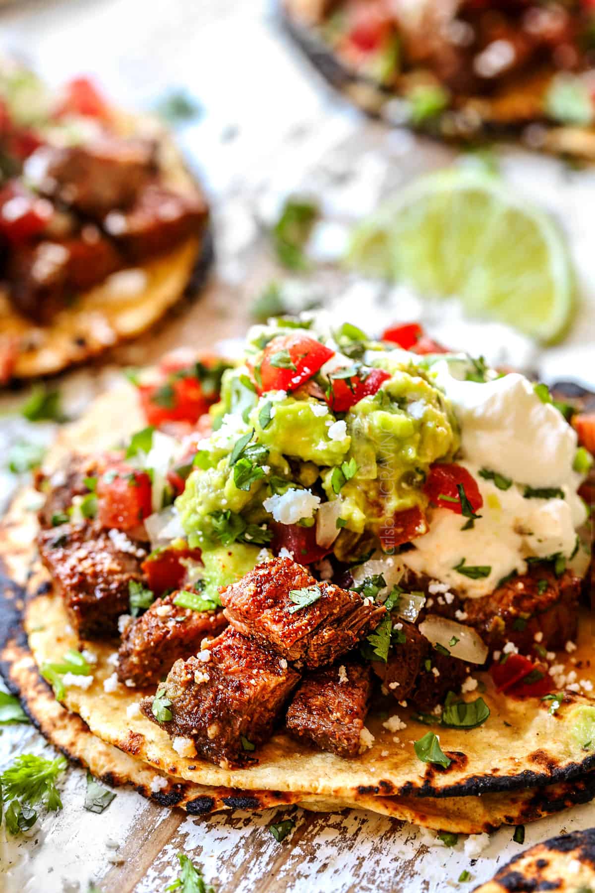 showing how to serve carne asada by chopping and adding to tortillas with guacamole, pico de gallo, and sour cream to make tacos