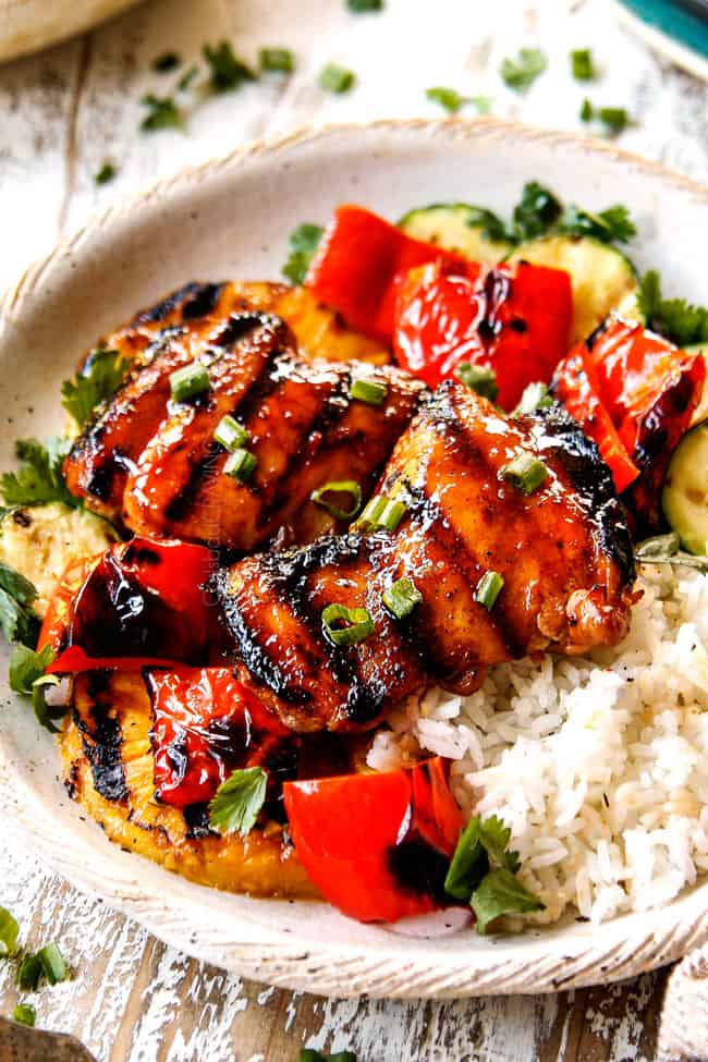 showing how to serve Hawaiian BBQ chicken by adding chicken to a cream plate with white rice and grilled bell peppers and zucchini