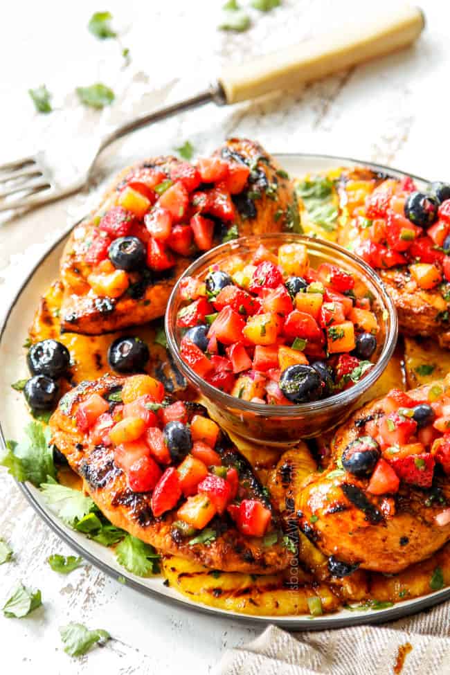 showing how to serve Hawaiian BBQ chicken by topping chicken on a white plate with strawberry salsa