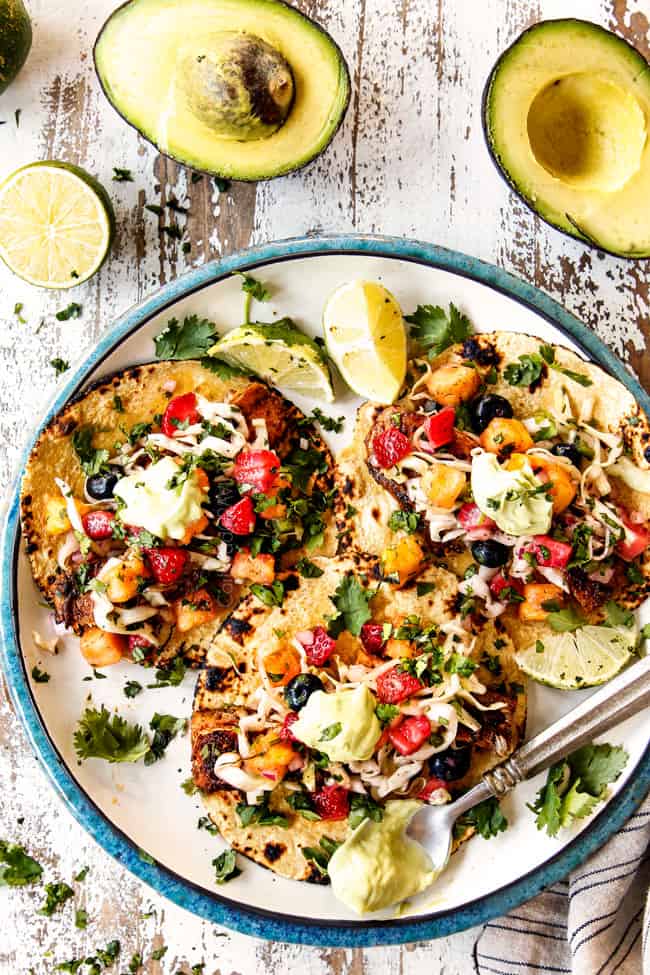 top view of mahi mahi fish tacos on a white plate with slaw and avocado crema