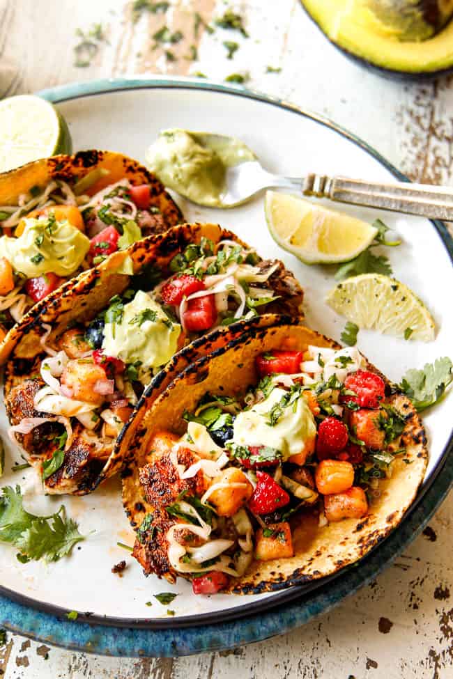 three mahi mahi fish tacos lined on a white plate with slaw and cilantro