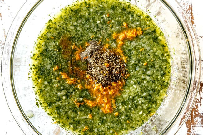 showing how to make steak marinade by adding orange juice, oregano, ground cumin, orange zest, finely chopping onion, garlic, cilantro and jalapeno to a large glass bowl