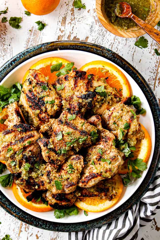top view of chicken marinated in mojo marinade on a white plate with orange slices showing what you can cook with mojo marinade