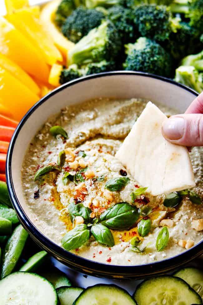 top view showing hummus recipe variation of pesto hummus by dipping a pita into the bowl of homemade hummus