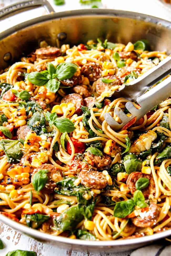 side view of serving spinach pasta by twirling pasta with tongs in a stainless steal skillet