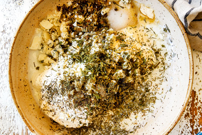 showing how to make steak salad recipe by adding dressing ingredients of mayonnaise, sour cream, chives, dill, parsley and blue cheese to a tan bowl