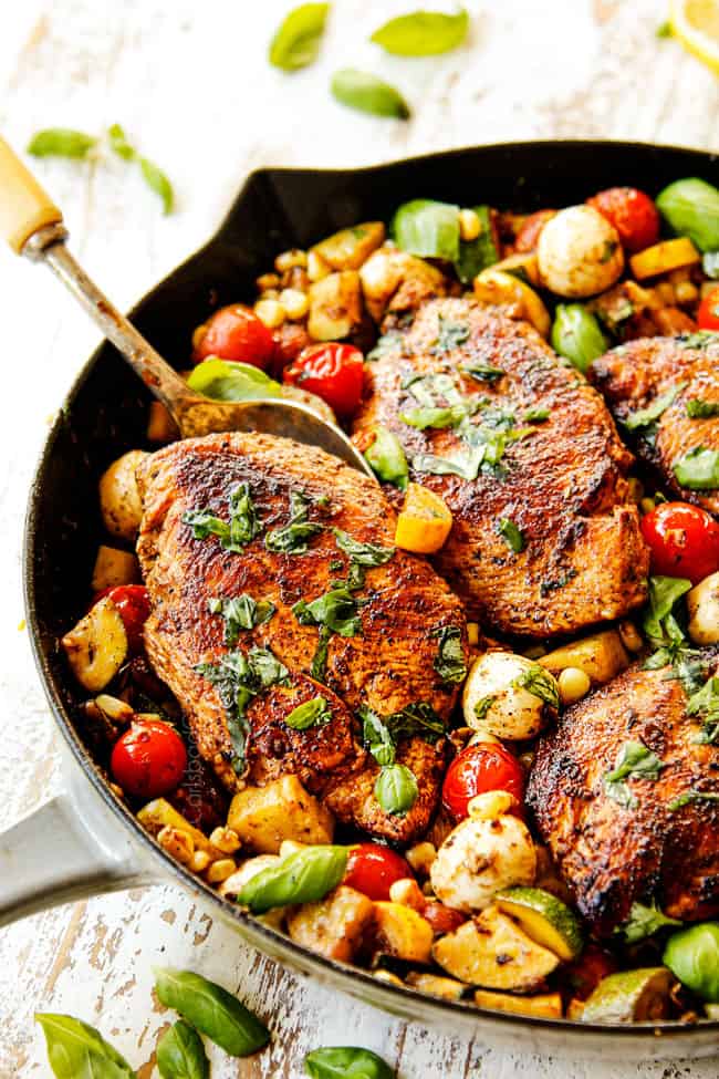 up close showing how to serve Tuscan Chicken by garnishing with basil and scooping chicken breast with a spoon