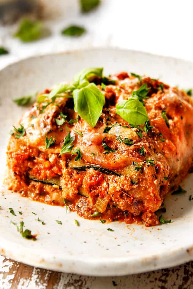up close of a slice of zucchini lasagna on a cream plate garnished with basil