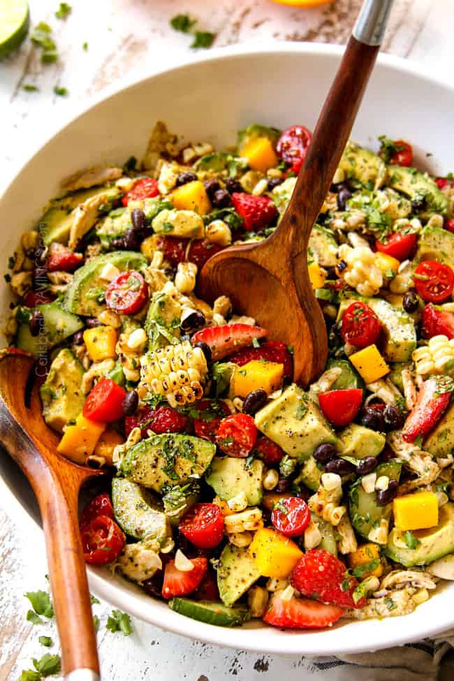 up close showing how to make serve avocado chicken salad by scooping up salad with wooden tongs