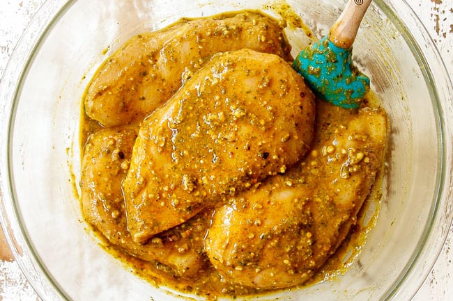 showing how to make Bruschetta Chicken recipe by marinating chicken in a glass bowl with pesto