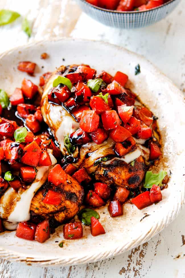 up close of chicken bruschetta recipe on a cream plate topped with melted mozzarella, bruschetta and balsamic glaze