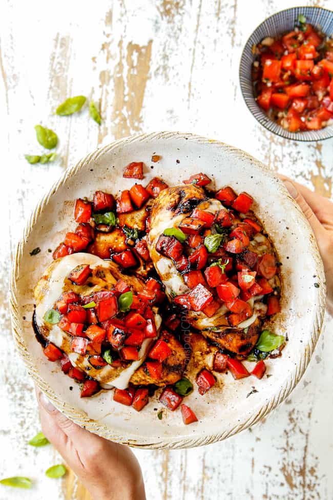 showering how to serve chicken bruschetta recipe with two hands holding plate of bruschetta chicken topped with tomato bruschetta