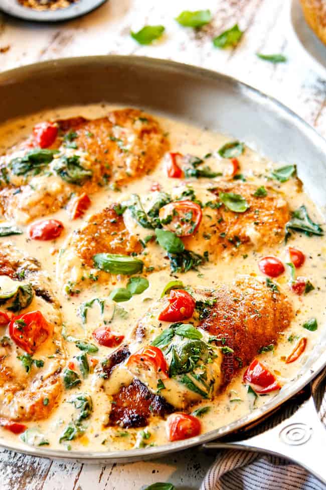 showing how to make Chicken Florentine by spooning cream spinach sauce over chicken cutlets in a stainless steel pan